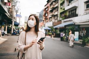 mujer soltera asiática joven de negocios usa máscara para el virus corona o covid19 en la ciudad al aire libre foto