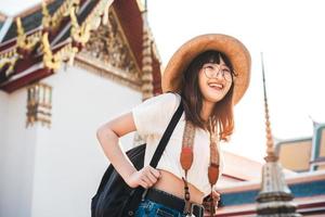 Young asian influence girl traveling in temple bangkok with camera and backpack. photo