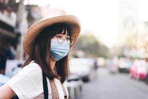 joven viajera asiática con gafas, sombrero y máscara protege el virus y el nuevo estilo de vida normal foto