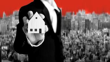 Business realtor man holding home model for investment on city background in black and white theme color. photo