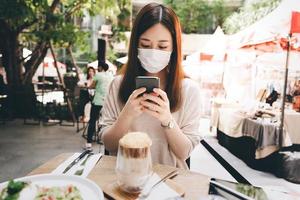 mujer asiática adulta joven usa máscara para un nuevo estilo de vida normal en un restaurante al aire libre el día foto