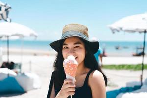 Young adult woman summer travel relax eating ice cream cone at outdoor beach cafe photo