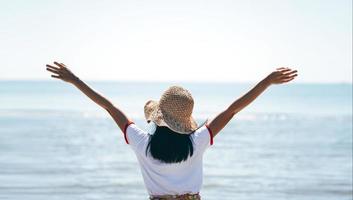 vista trasera de una joven asiática adulta que estira la mano y el brazo abierto se relaja en la playa. foto