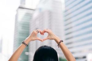 vista trasera de una mujer soltera mano arriba con gesto de corazón usar accesorio de plata. foto