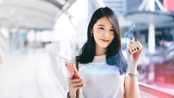 Young adult business working asian woman holding mobile phone and house model for online insurance application with digital finance graph. photo