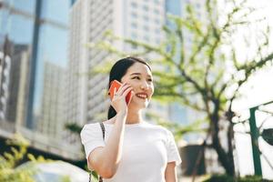 Happy young adult asian business single woman use mobile phone talking with friend city background.