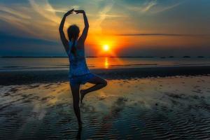 chica hace el saludo al sol al amanecer en la playa foto