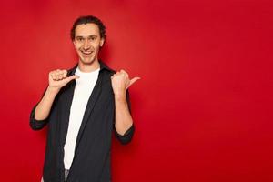 studio portrait of handsome smiling, joyful man thumbs up to an empty free area behind him, dressed in casual clothes, blue shirt isolated on red background. concept - people, recommendation, approval photo