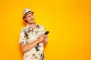 male tourist traveler on vacation writes message on phone with funny facial expression looking to side with his tongue sticking out. isolated on yellow background space for text. concept communication photo