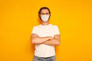 man in protective medical mask and casual clothes crossed his arms over his chest as sign of dissatisfaction isolated on yellow background. concept of people, medicine, protection from covid19 virus