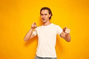 young, joyful, curly-haired man points his index fingers in front of him, hinting that you are best, winner. isolated yellow background with space for text. concept people, victory, advantage, delight
