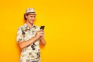 a male tourist on vacation with a smartphone in his hands writes a message and smiles. isolated on a yellow background. space for text. concept of people, recreation, communication in social networks photo