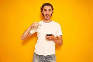 young man in casual clothes received joyful message about victory, winning discounts, pointing to phone with finger with surprised happy face. concept people, technologies, advertising. space for text photo