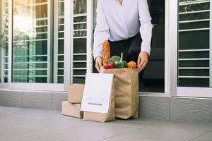 Asian woman open the door and took the bag of food ordered by the carrier to put in front of the house to prevent the epidemic. photo