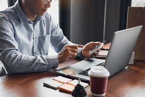 las manos del hombre sostienen teléfonos inteligentes y usan computadoras portátiles que ingresan a sitios web para comprar productos. foto