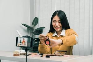 Beautiful asian woman blogger using camera phone recording vlog video live streaming and showing how to make up cosmetics at home. photo