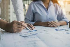 Architects engineer working with blueprints on table and discussing project together at the meeting in the office. photo