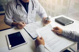 Confident doctor man holding a pill bottle and talking with senior patient and reviewing his medication at office room. photo