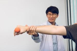 Fisioterapeuta masculino joven asiático que ayuda al paciente con ejercicios de levantamiento de pesas en la clínica. foto