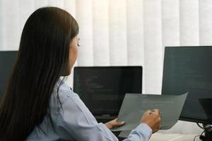 Asian woman software developers sitting in front of computers looking at computer codes on the screen. photo