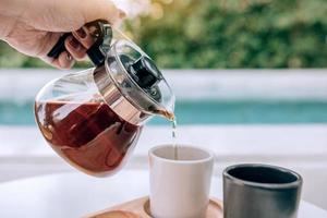 Woman's hand holding a coffee mug and pouring it into the coffee cup. photo