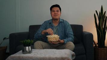 hombre asiático viendo una serie de sala de estar mientras come palomitas de maíz por la noche. foto