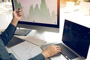 Two investors are working together with analyzing the stock data graphs in the paper and viewing the data on the laptop screen. photo