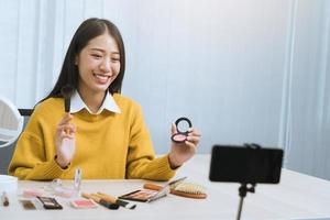 Young asian woman vlogging herself about beauty products with making a video for her blog on cosmetics using phone camera at home. photo