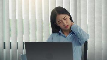 una joven asiática está sentada en una oficina corporativa y tiene dolor en el cuello. foto