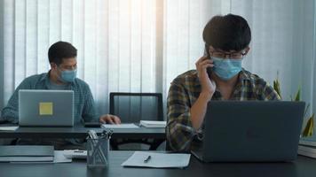 Asians sit in their office and use the phone to talk to clients while wearing masks in their offices during COVID-19. photo