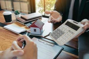 los agentes están calculando la tasa de pago del préstamo o el monto de las primas de seguro para los clientes que vienen a ponerse en contacto con la compra de una nueva casa en la oficina. foto