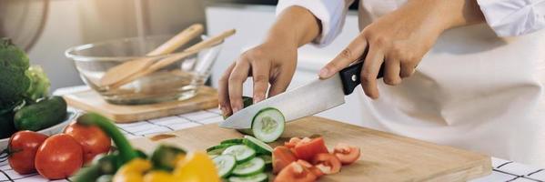 Woman using knife and hands cutting cucumber on wooden board in kitchen room. photo