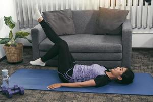 Asian woman practicing yoga at home while lying on a mat and stretching her legs.