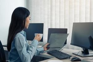 Asian woman was drinking coffee in the early morning while contemplating the program and code on the computer screen. photo