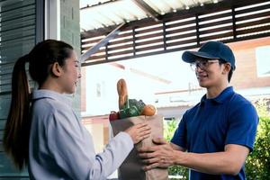 repartidor asiático entregando una bolsa de papel dentro con verduras o comida a una mujer asiática frente a su casa. foto
