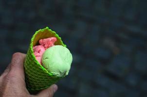 un hombre que sostiene un tubo verde de helado de fresa y pistacho sobre un fondo de pavimento de piedra gris. primer plano, espacio para texto. foto