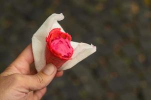 un hombre que sostiene un cono de helado rasberry en una servilleta en la calle. el cono de helado se come parcialmente. foto