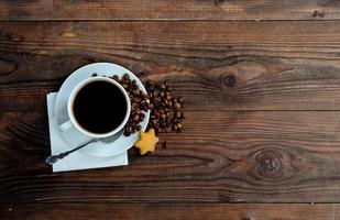 una taza de café, granos de café y galletas de una estrella sobre fondo de madera oscura. foto
