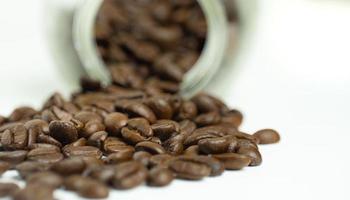 roasted coffee beans Get ready for the grind being poured out of a glass bottle laid on a white background To make fresh coffee or go into an espresso machine or Moka Pot photo