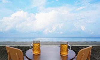 Draft or craft beer in a tall clear glass With beer foam on top And there are bubbles in the glass. Cold beer in a glass, placed on a wooden table on the beach, the sea during the day. 3D Rendering photo