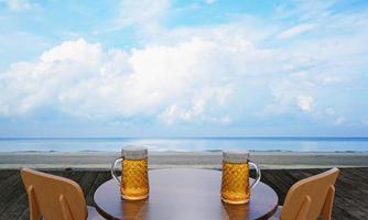 cerveza artesanal o de barril en un vaso transparente alto con espuma de cerveza encima y burbujas en el vaso. cerveza fría en un vaso, colocada sobre una mesa de madera en la playa, el mar durante el día. representación 3d foto