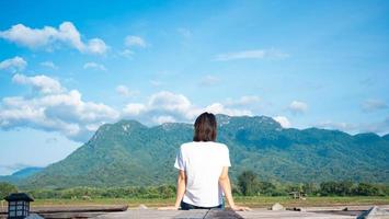 girl wearing a casual t-shirt Sit on a wooden walkway, see nature, mountains, rice fields, fresh air. and the morning sun bright blue sky white clouds photo