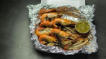 Grilled Shrimp with Seafood Sauce Contained in aluminum foil food wrap and foam food container. Thai style seafood sauce, spicy and sour taste, main ingredient, lime juice, fresh chili, fish sauce photo
