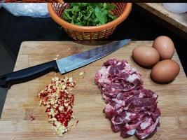 Cooking ingredients name Stir-fried basil beef with a fried egg. And chopped fresh chilies with garlic Place on a wooden chopping board with a knife. Holy basil leaves in an orange basket photo