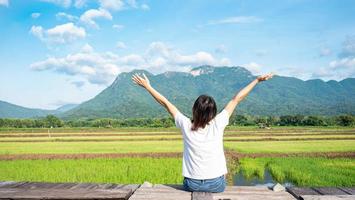 The girl held up two hands and breathed fresh. show independent symptoms Sit by a wooden bridge on a rice field, nature, clear air. Grasslands, mountains, and clear skies. photo