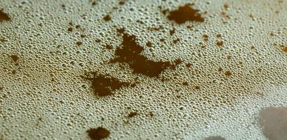 Air bubbles or foam on the front surface of the beer in the glass. The beer glass has water and bubbles on the edge of the glass. photo