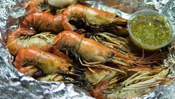 camarones a la parrilla con salsa de marisco envueltos en papel de aluminio y en un recipiente de espuma para alimentos. salsa de mariscos al estilo tailandés, sabor picante y agrio, ingrediente principal, jugo de lima, chile fresco, salsa de pescado foto