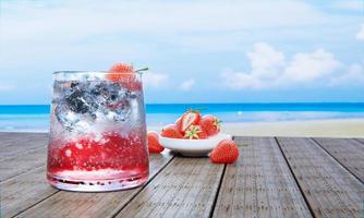 soda de fresa con cola sin alcohol no mezcle alcohol. fresas frescas en un tazón de cerámica en el fondo se desdibujan en una mesa de madera. restaurante en la playa y el mar. Bebidas frescas de jugo con cubitos de hielo. representación 3d foto