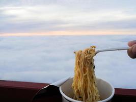 Instant noodles in a cup And white forks Background image of the sea fog in the morning before sunrise. photo