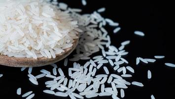 Jasmine rice, popular rice variety in Thailand. Rice grain that has passed through the polishing process Ready to be cooked or steamed. White seeds on black background. photo